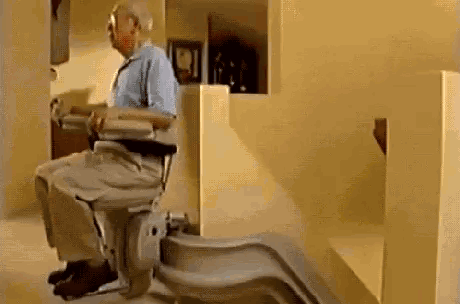 An Elderly Man Is Sitting On A Stair Lift In A House . GIF