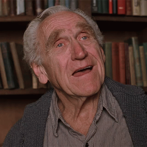 An Elderly Man Making A Funny Face In Front Of Bookshelves GIF
