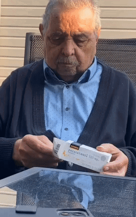 An Elderly Man Sitting At A Table Looking At A Box Of Paracetamol GIF
