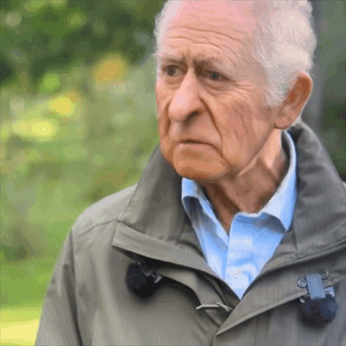 An Elderly Man Wearing A Grey Jacket And Blue Shirt GIF