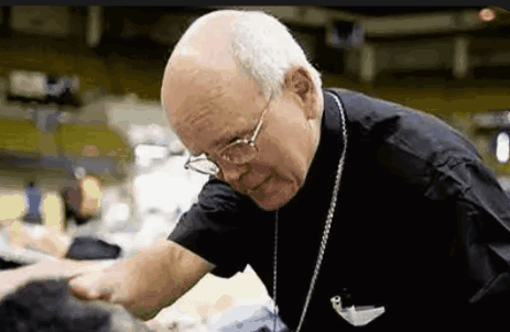 An Elderly Man Wearing Glasses And A Black Shirt Is Talking To A Group Of People . GIF