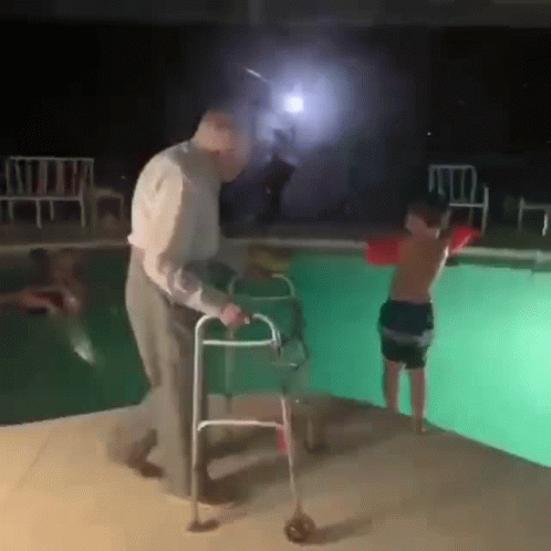 An Elderly Man With A Walker Is Helping A Young Boy With A Life Preserver Into A Swimming Pool . GIF