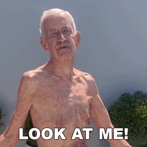 An Elderly Man Without A Shirt Is Standing In Front Of A Sign That Says Look At Me GIF