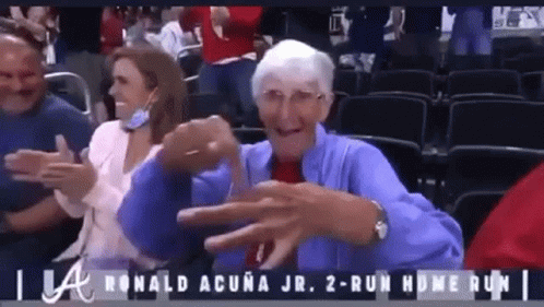 An Elderly Woman In A Blue Jacket Is Sitting In A Stadium Watching A Baseball Game .. GIF