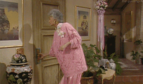 An Elderly Woman In A Pink Dress Is Opening A Door GIF