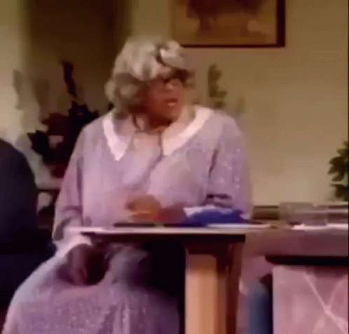 An Elderly Woman In A Wig Is Sitting At A Table . GIF