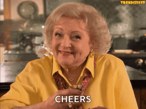 An Elderly Woman In A Yellow Shirt Is Holding A Glass Of Whiskey And Says Cheers GIF