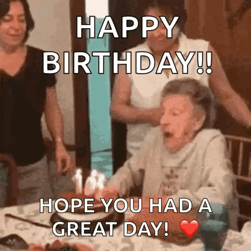 An Elderly Woman Is Blowing Out Candles On A Birthday Cake While Sitting At A Table . GIF