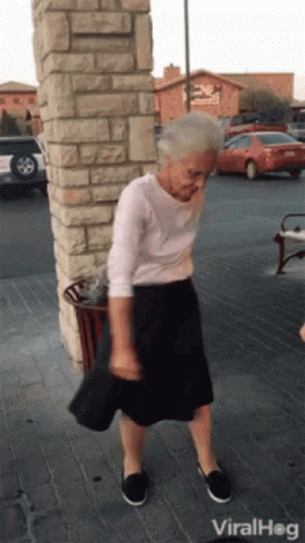 An Elderly Woman Is Dancing In Front Of A Brick Wall And A Sign That Says Viral Hog GIF