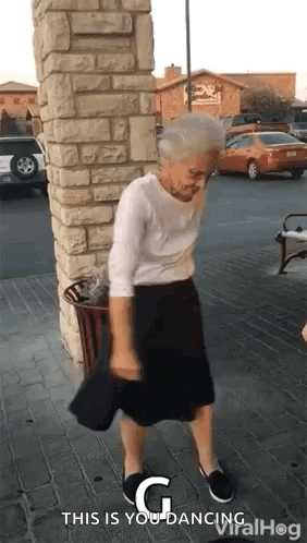 An Elderly Woman Is Dancing On The Sidewalk In Front Of A Brick Building . GIF