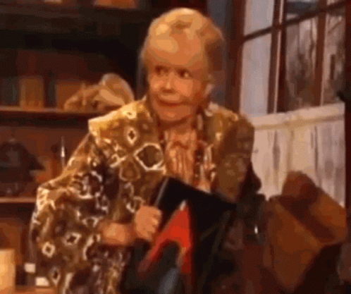 An Elderly Woman Is Holding A Book And Smiling While Sitting In Front Of A Window . GIF