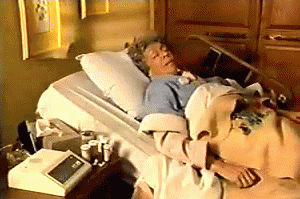 An Elderly Woman Is Laying In A Hospital Bed With A Thermometer On The Table GIF