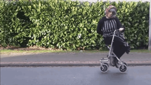 An Elderly Woman Is Riding A Walker On The Street GIF