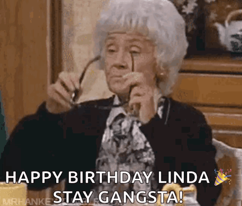 An Elderly Woman Is Sitting At A Table Holding Glasses And Saying Happy Birthday Linda Stay Gangsta ! GIF