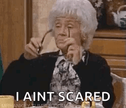 An Elderly Woman Is Sitting At A Table Holding Glasses And Says `` I Ain T Scared '' . GIF