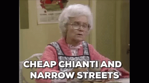 an elderly woman is sitting at a table with a plate of food and saying `` cheap chianti and narrow streets `` .