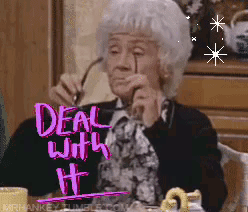 An Elderly Woman Is Sitting At A Table With A Sign That Says Deal With It On It GIF