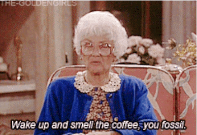 An Elderly Woman Is Sitting In A Chair And Says Wake Up And Smell The Coffee You Fossil GIF