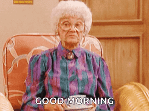 An Elderly Woman Is Sitting In A Chair Holding A Cup Of Coffee And Saying " Good Morning " GIF