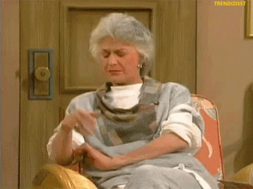 An Elderly Woman Is Sitting In A Chair With Her Hands Folded . GIF
