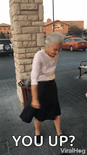 An Elderly Woman Is Standing In Front Of A Brick Wall With The Words " You Up " On The Bottom GIF