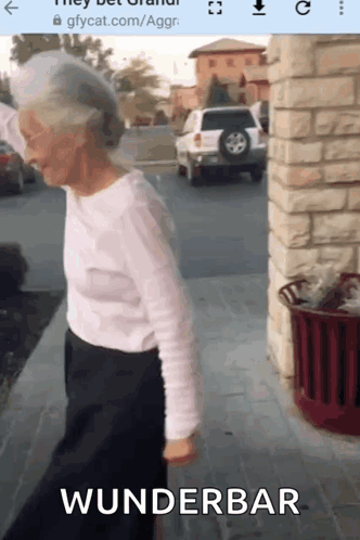 An Elderly Woman Is Walking Down A Sidewalk With The Word Wunderbar On The Bottom Of The Screen . GIF
