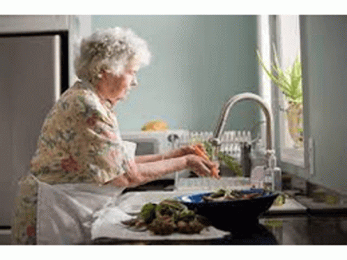 An Elderly Woman Is Washing Vegetables In A Sink In A Kitchen . GIF