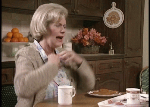 An Elderly Woman Sitting At A Table With A Cup Of Coffee GIF
