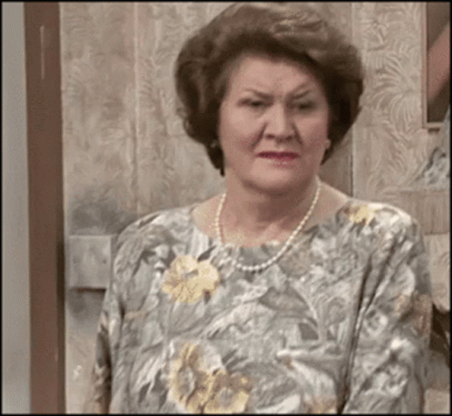 An Elderly Woman Wearing A Pearl Necklace And A Floral Shirt GIF