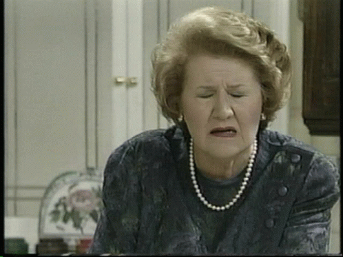 An Elderly Woman Wearing A Pearl Necklace And Earrings Makes A Funny Face GIF