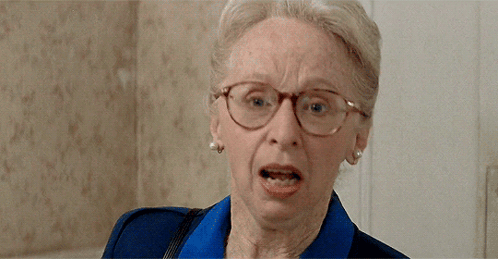 An Elderly Woman Wearing Glasses And A Blue Shirt Is Making A Funny Face GIF