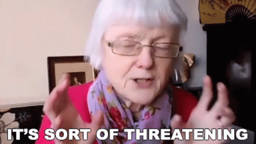 An Elderly Woman Wearing Glasses And A Scarf Is Making A Threatening Gesture . GIF