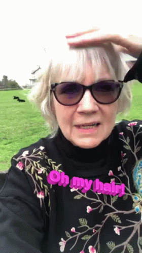 An Elderly Woman Wearing Sunglasses And A Black Shirt Says Oh My Hair GIF