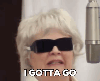 An Elderly Woman Wearing Sunglasses And A Wig Is Standing In Front Of A Microphone . GIF