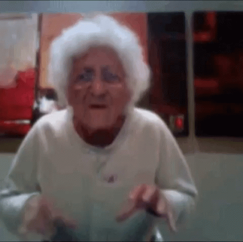 An Elderly Woman With Gray Hair Is Standing In Front Of A Wall . GIF