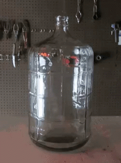 An Empty Glass Bottle Sits On A Table In Front Of Tools GIF