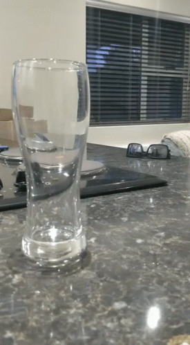 An Empty Glass Sits On A Kitchen Counter Next To A Pair Of Sunglasses GIF