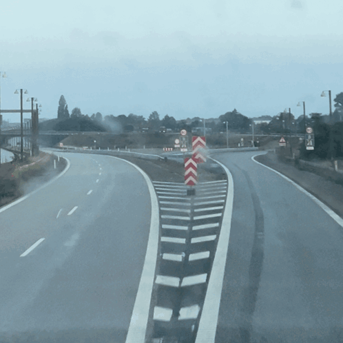 An Empty Highway With A Red And White Chevron Sign In The Middle GIF