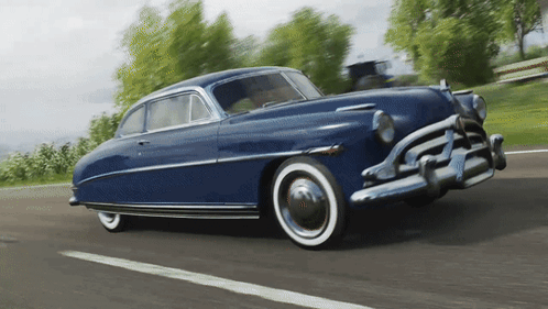 An Old Blue Car With White Tires Is Driving Down The Road GIF