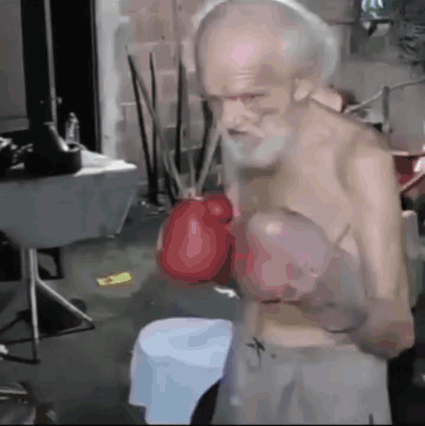 An Old Man With A Beard Is Wearing Boxing Gloves In A Room GIF