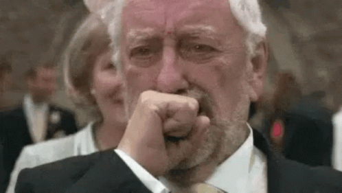 An Older Man In A Suit And Tie Is Crying While Covering His Mouth With His Hand . GIF