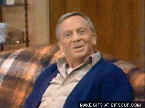 An Older Man Is Sitting On A Couch And Smiling . GIF