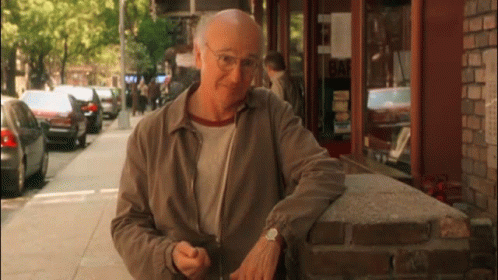 An Older Man Leans Against A Brick Wall In Front Of A Building That Says Bar GIF