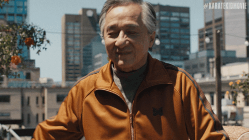 An Older Man Wearing An Orange Jacket With The Hashtag #Karatekidmovie On The Bottom GIF