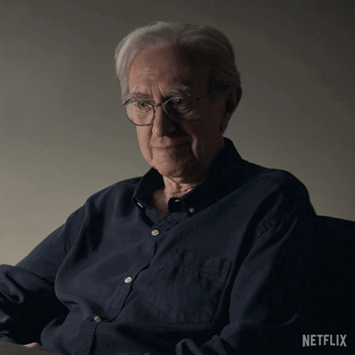 An Older Man Wearing Glasses And A Blue Shirt With The Netflix Logo On The Bottom GIF