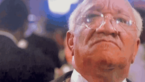 An Older Man Wearing Glasses And A Tuxedo Is Looking At The Camera . GIF