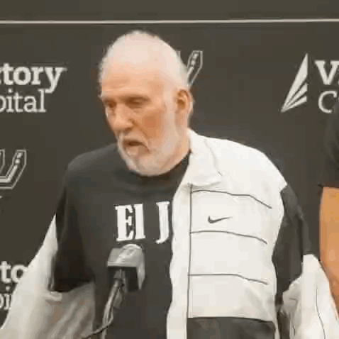 An Older Man With A Beard Is Standing In Front Of A Microphone . GIF