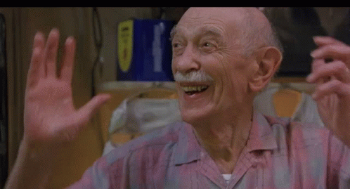 An Older Man With A Mustache Is Smiling And Waving His Hands In A Kitchen . GIF