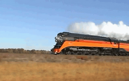 An Orange And Black Train Is Going Down A Track GIF