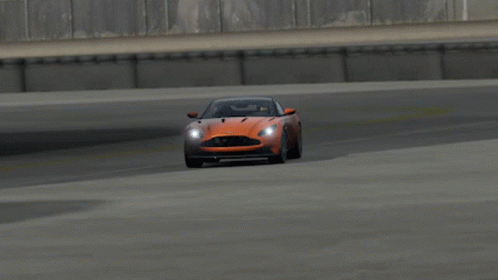 An Orange Aston Martin Sports Car Is Driving On A Track GIF